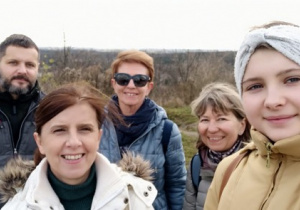 Pięć uśmiechniętych postaci pozuje do zdjęcia. W tle jesienna panorama Łodzi.